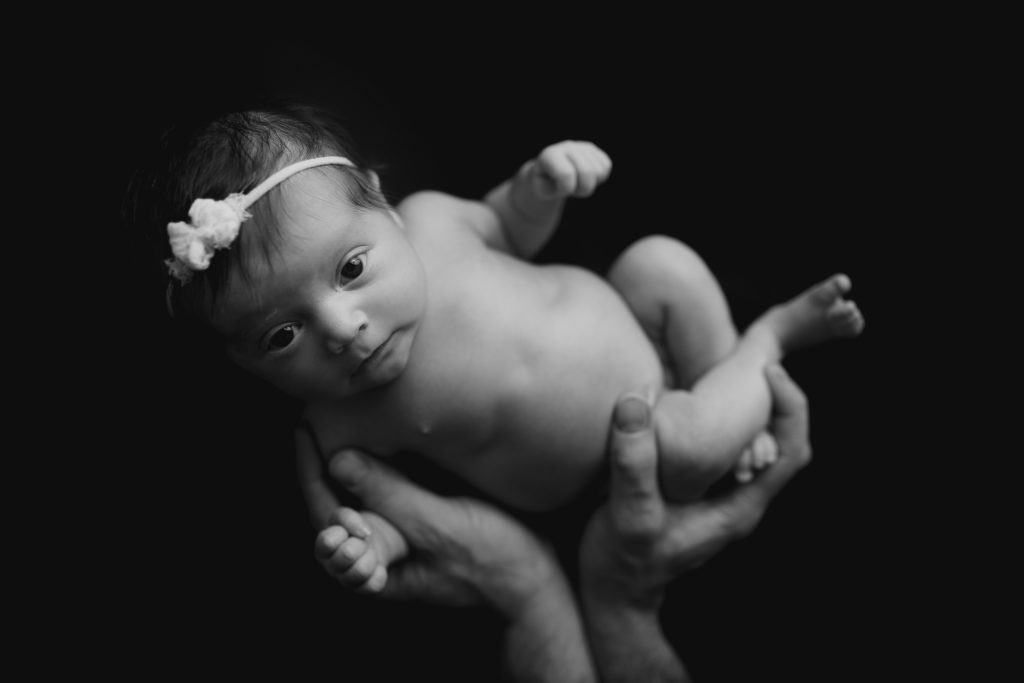 Black and white photo of newborn baby in dad's hands